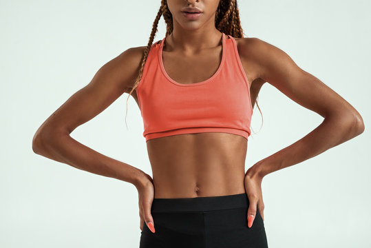 Perfect body. Cropped photo of muscular young african woman in sportswear keeping arms on hips while standing against grey background