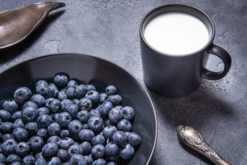 Obraz na płótnie Canvas Fresh blueberries in black ceramic bowl with cup of milk
