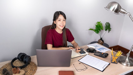 A young, beautiful relaxing business asian girl use a laptop working remotely from home on desk as a freelancer, quarantine for Coronavirus and smart working concept.