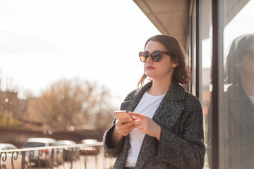 portrait of a young girl in sunglasses holding a smartphone on the street