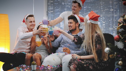 Friends of different race celebrating Christmas in confetti blowing while making cheers and blowing party whistles at home.