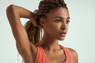 Perfect body. Close up of beautiful young african woman in sportswear holding her hair in hand and looking away while standing against grey background