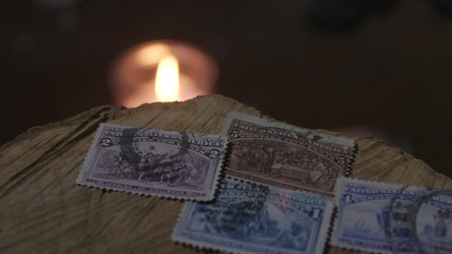 Old Us stamps from a stamp collection on a wooden log with a candle burning in the back ground.