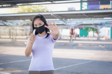 Fototapeta premium Selective focus on the eyes of a young Asian woman wears a protective black mask and holds a spray hand sanitizer, blurred left-hand shows the symbol to stop Covid-19 with the concept of healthcare.