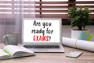 Laptop with phrase ARE YOU READY FOR EXAMS on wooden table in office