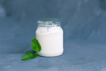 Yogurt in a glass package with mint leaves on a dark gray background. Healthy Nutrition, Essential Dairy Products