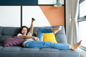 Beautiful bored brunette girl on the couch in a stylish interior is watching TV. Switches the TV...