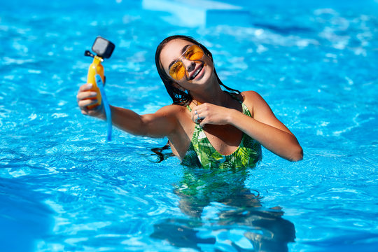 Travel blogger woman taking selfie photo with action camera in a swimming pool. Lifestyle vlogger films vlog from luxury resort on sunny day. Hot girl in swimsuit live streaming for social media likes