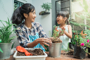 happy excited mother and her daughter gardening together plants some flower at home