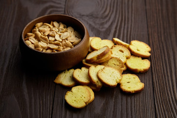 Bruschette chips, roasted peanuts in a bowl, salty beer snacks on wooden background