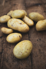 New potatoes, characteristic for their thin skin, are harvested when the ripening is not complete. In the photo potatoes on wooden table