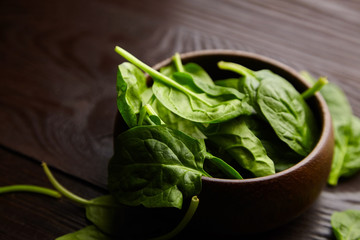Spinach fresh green leaves in a bowl on wooden background