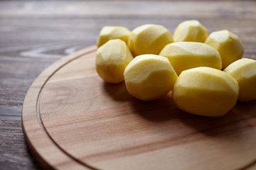 Potatoes on wooden cutting board on brown table. Root vegetable. Uncooked whole peeled potatoes