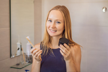 young woman brushing her teeth with a black tooth paste with active charcoal, and black tooth brush in her bathroom