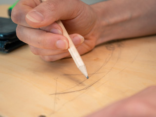 Artist sketching on a wooden object. Soft pastel colours with natural lighting. Female hand holding a pencil. 