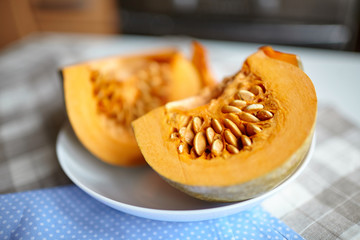 Pumpkin slices on a white plate on a table with blue napkin. Fresh pieces of pumpkin with seeds