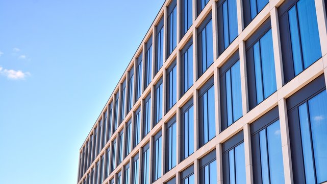 Modern office building windows with vertical lines and reflection. Building reflecting the sky with clouds and creating a surreal view.