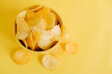Potato chips in a yellow bowl on a yellow background. Top view. Copy, empty space for text