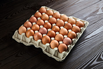 Egg tray on wooden background. Brown chicken eggs in recycled cardboard package on table