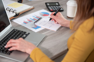 Woman taking notes while using laptop