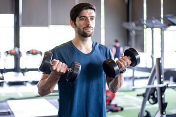 Healthy Caucasian man lifting dumbbells in the gym with smile and fresh face. Exercise, workout, muscle training, weight lifting, weight loss, heart rate practice and diet concept.