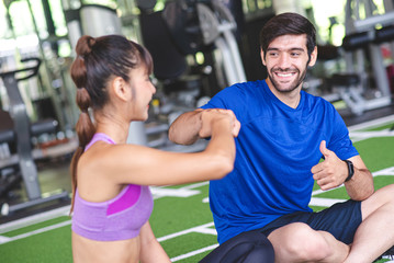 Fototapeta na wymiar Caucasian man are punching hand and thumb up with his Asian woman friend in the gym after exercise cardio muscle training with smile and fresh face. Healthy care, body muscle builder concept.