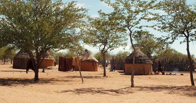 Himba tribe village with people walking around, sunny day, Namibia, 4k