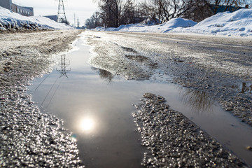 road with spring streams that flow along the road covered with ice and dense snow, reflection of...