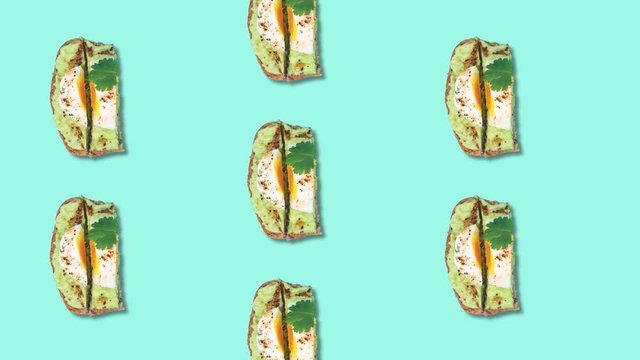 Pattern eating avocado toast with poached egg, spices and cilantro leaf. Loop stop motion animation. Healthy food concept, Tiffany blue background, top view.