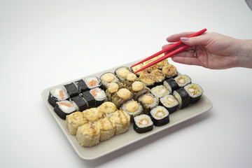 Rectangular plate full of sushi rolls and sticks of red color, on an isolated background, close-up.