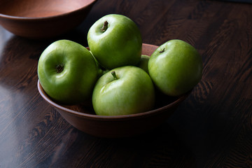 Green apples in a plate on a brown wooden table.