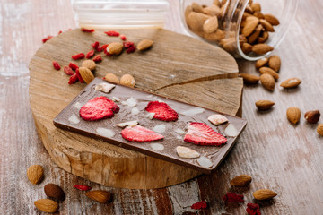 Sweet bar of chocolate with fruits and nuts on the wooden background