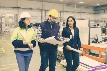 Factory employees walking with blueprint at printing house. Concentrated workers checking quality...