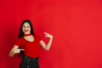 Pointing at herself. Caucasian young woman's monochrome portrait isolated on red studio background. Beautiful female brunette model. Concept of human emotions, facial expression, sales, ad.
