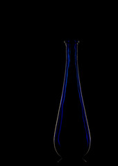 Elegant blue glass vase, backlit, silhouetted on black background.