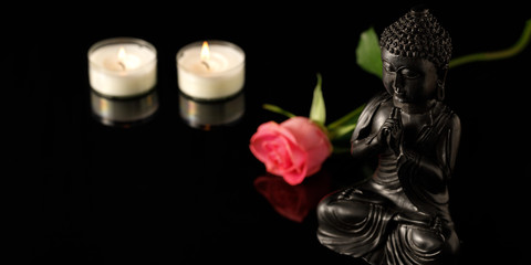 Buddha with burning candles und rose in glass black background. Spa or meditation