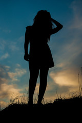 Silhouette of a tall girl against the sky with an evening sunset. A girl in a skirt stands on a...