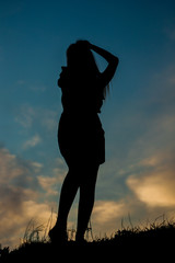 Silhouette of a tall girl against the sky with an evening sunset. A girl in a skirt stands on a mound with long hair and a short skirt.
