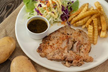 The plate of grilled pork steak with side dish french fries and salad. Decorated with potatoes on the wooden table