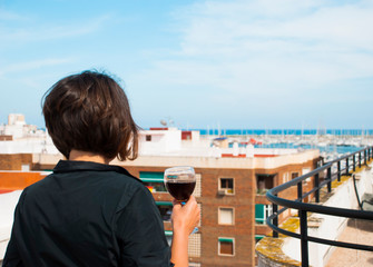 Woman look from her balcony on sea in Spain with glass of red wine. Woman in stress.