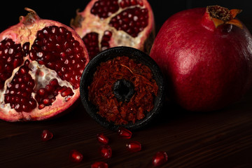 A hookah smoking bowl filled with red pomegranate flavor tobacco lies next to a whole and cut pomegranate on a dark brown wooden background. smoke hookah