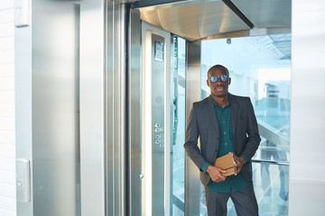 Portrait of African young businessman in eyeglasses standing in the elevator of office building and...