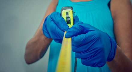 Conceptual photo of social distancing during Coronavirus crisis.  Selective focus on the yellow tape measure. and the gloves.  Blurry background of a black woman maintaining a safe distance.