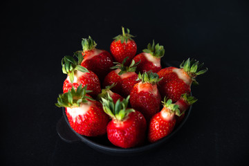 Fresh juicy strawberries in a black plate on a black matte background