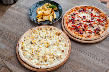 two pizzas and fried potatoes stand on a wooden table