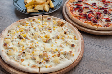 two pizzas and fried potatoes stand on a wooden table