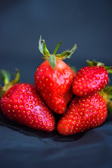 Vertical picture of fresh wet strawberries on dark black crumpled paper background. Spring summer vegetarian vegan food. Vitamins in fresh berries. Organic healthy fruits. Selective focus. Defocused