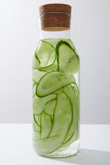 Glass bottle with cork filled with water and sliced cucumbers isolated on grey