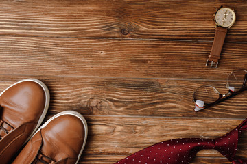 Top view of mens beige casual shoes, polka dots red tie, wristwatch and glasses on wooden background
