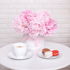 Morning breakfast - cup of coffee and macaroons with vase of pink peonies on the white table